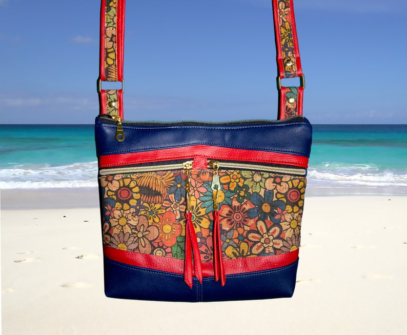 May include: A blue crossbody bag with a red strap and a floral print. The bag has two zippered pockets and a tassel.