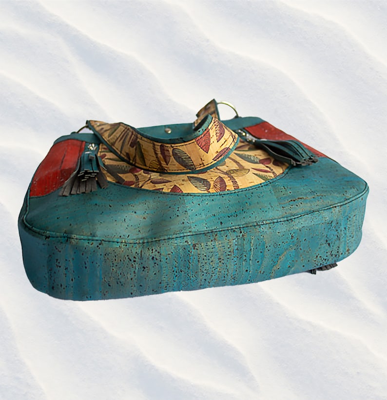 May include: A teal blue cork handbag with a yellow and red floral pattern. The bag has a long strap and a tassel on the side.
