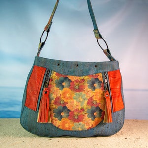 May include: A blue cork handbag with a floral print and orange leather accents. The bag has two zippered pockets and a tassel on each zipper pull.