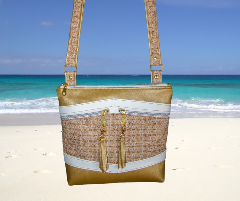 May include: A gold and white crossbody bag with a woven fabric design and gold tassel zipper pulls. The bag is photographed against a beach background.