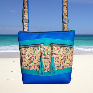 May include: A blue crossbody bag with a cork and floral print panel. The bag has two zippered pockets and a turquoise trim.
