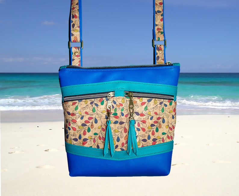 May include: A blue crossbody bag with a cork and floral print panel. The bag has two zippered pockets and a turquoise trim.