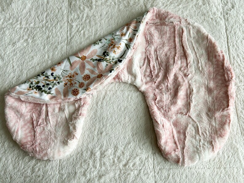 以下が含まれることがあります： 花柄のピンクと白のベビー用おくるみ。おくるみは柔らかく、ふわふわした生地で作られており、赤ちゃんを暖かく快適に保つように設計されています。