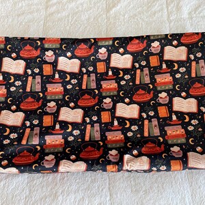 May include: A dark blue fabric with a repeating pattern of teapots, books, teacups, candles, moons, and flowers in shades of red, orange, and white. The fabric is likely used for crafting or home decor.