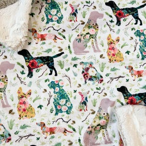 May include: White blanket featuring a pattern of different dog breeds, each filled with floral designs in pink, yellow, and blue. The blanket has a soft, plush texture with a white, textured border.