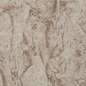 May include: Close-up of a plush, textured fabric in a neutral, light taupe color. The surface has a soft, wavy pattern, resembling fur or a luxurious textile. The overall appearance is warm and inviting.