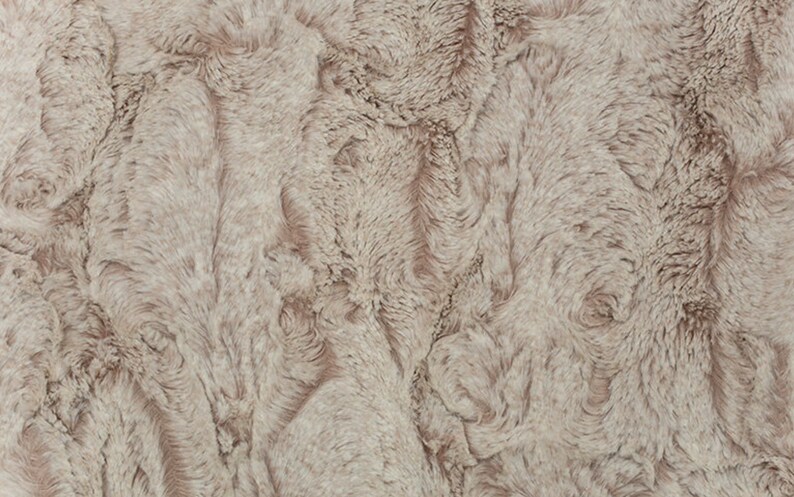 May include: Close-up of a plush, textured fabric in a neutral, light taupe color. The surface has a soft, wavy pattern, resembling fur or a luxurious textile. The overall appearance is warm and inviting.