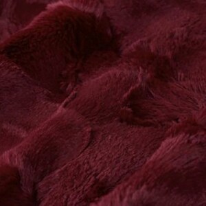 May include: Close-up of a plush, burgundy fabric with a textured, rippled surface. The material has a soft, furry appearance, with visible fibers and a deep, rich color. The fabric's folds create shadows and highlights.