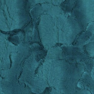 May include: A close-up of a teal-colored fabric with a plush, textured surface. The fabric has a soft, fur-like appearance with varying shades of teal and darker areas, creating a dimensional effect. The material appears to be a faux fur or similar textile.