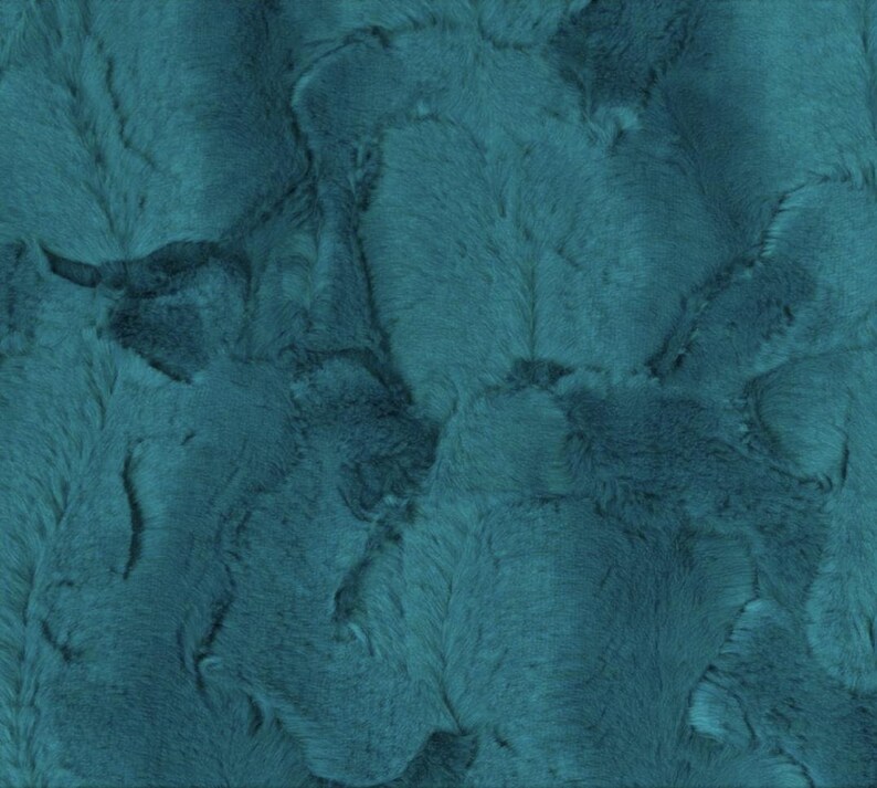May include: A close-up of a teal-colored fabric with a plush, textured surface. The fabric has a soft, fur-like appearance with varying shades of teal and darker areas, creating a dimensional effect. The material appears to be a faux fur or similar textile.