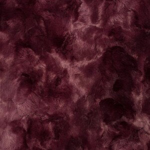 May include: Close-up of a plush fabric with a deep burgundy color and a textured, fur-like appearance. The fabric has a soft, luxurious look, with lighter shades of burgundy and pinkish hues interspersed throughout.
