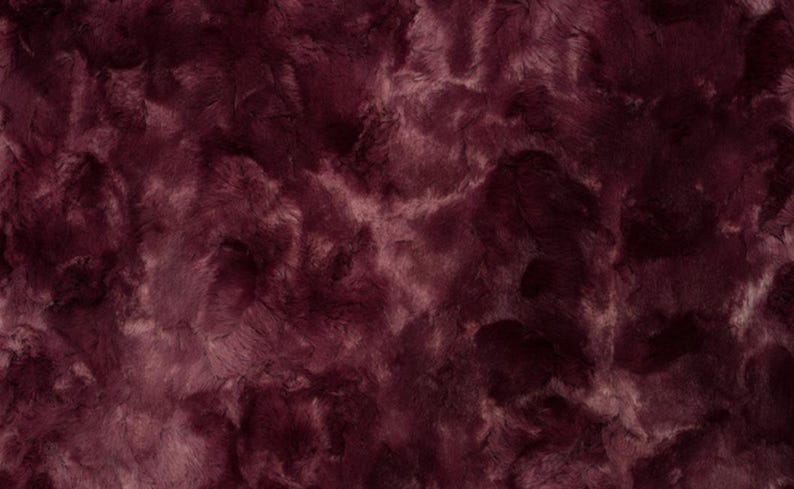 May include: Close-up of a plush fabric with a deep burgundy color and a textured, fur-like appearance. The fabric has a soft, luxurious look, with lighter shades of burgundy and pinkish hues interspersed throughout.