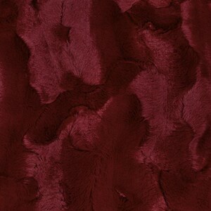 May include: Close-up of a burgundy faux fur fabric. The plush material has a wavy, textured pattern with varying shades of the deep red color. The fabric appears soft and luxurious, suitable for various craft projects.