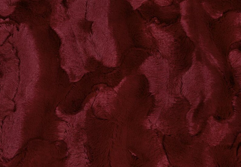 May include: Close-up of a burgundy faux fur fabric. The plush material has a wavy, textured pattern with varying shades of the deep red color. The fabric appears soft and luxurious, suitable for various craft projects.