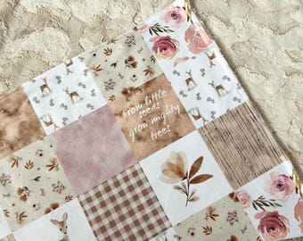 Puede incluir: Una manta de bebé de patchwork con una variedad de patrones, incluyendo flores, ciervos y veta de madera. La manta está en tonos de marrón, rosa y blanco. El texto "From little seeds grow mighty trees" está impreso en uno de los cuadrados.