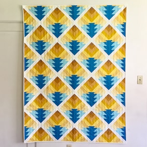 May include: A quilt with a geometric pattern of blue, yellow and white triangles. The quilt is made up of repeating diamond shapes.