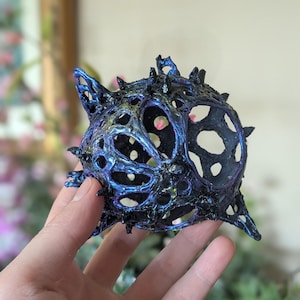 May include: A dark blue and iridescent, 3D printed, sphere-shaped object with a hollow center and a spiky, organic-looking exterior.