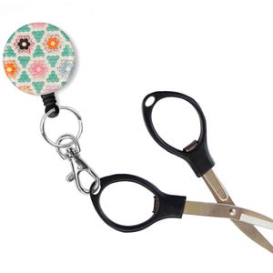 May include: A black retractable keychain with a colorful patterned button and a pair of black handled scissors with silver blades.