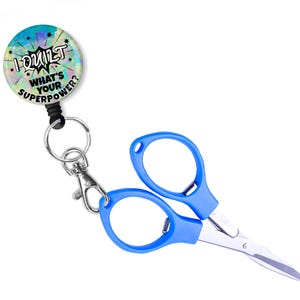May include: A blue retractable badge reel with a round button that says "I Quilt What's Your Superpower?" and a pair of blue handled scissors attached to the reel.