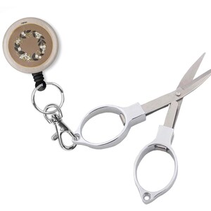 May include: A silver retractable keychain scissors with a floral design on the retractable reel. The scissors have a small loop for attaching to a keychain.
