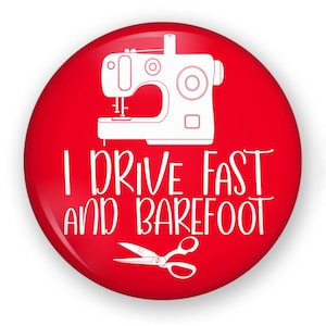 May include: A circular red pinback button featuring a white line art illustration of a sewing machine at the top, a pair of scissors at the bottom, and the white text I DRIVE FAST AND BAREFOOT centered between the two icons.