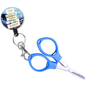 May include: A blue retractable badge holder with a key ring and a round button that says "YES I really do NEED all this FABRIC". A pair of blue handled scissors with a silver blade is attached to the key ring.