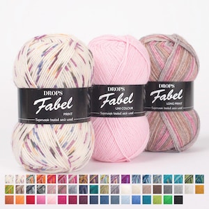Puede incluir: Tres ovillos de hilo Drops Fabel en varios colores. Uno es un estampado con una mezcla de colores, otro es rosa liso y el tercero es un estampado largo con tonos rosas y marrones. También se muestra una carta de colores.