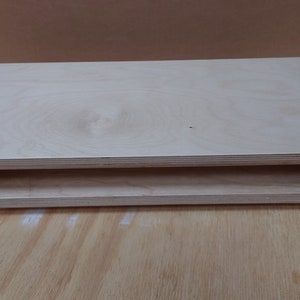 May include: A light wood shelf unit with a single shelf. The shelf is made of plywood and has a natural finish. The shelf is supported by black metal brackets.