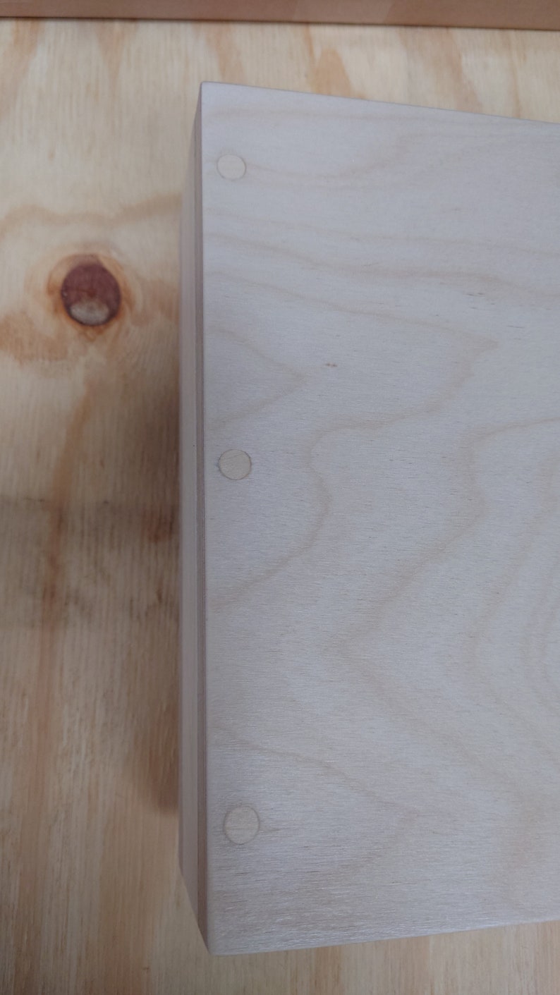 May include: A light wood box with three round wooden plugs on the top.