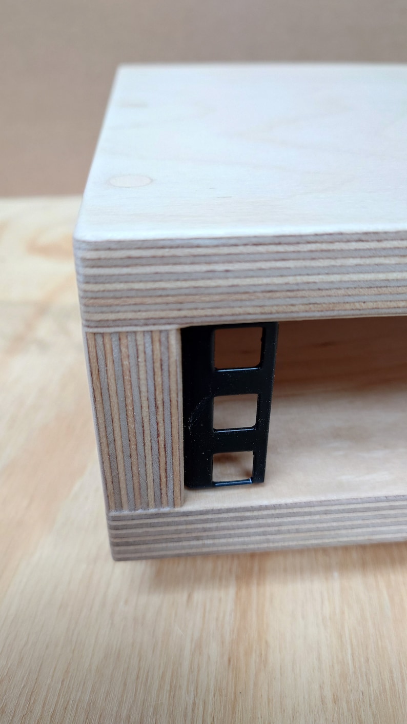 May include: Close-up of a wooden shelf with a black metal rack mounted on the side. The shelf is made of plywood with visible layers of wood veneer.