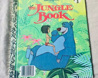 May include: A Little Golden Book titled "The Jungle Book." The cover features a blue bear and a boy in red shorts, set against a green jungle background. The book has a yellow top and a white barcode.