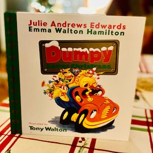 May include: A hardcover children's book titled "Dumpy Saves Christmas" by Julie Andrews Edwards, Emma Walton Hamilton, illustrated by Tony Walton. The cover features a cartoon car with characters and the title in red.