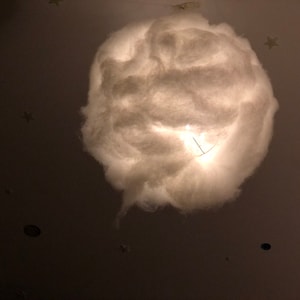 May include: A white fluffy cloud-shaped lampshade with a light bulb inside, hanging from a ceiling.
