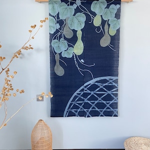 Könnte beinhalten: Ein dunkelblauer Wandbehang aus Stoff mit einem Design aus Kürbissen und Blättern in Grün- und Blautönen. Der Behang hat unten ein gewebtes Kreisdesign.