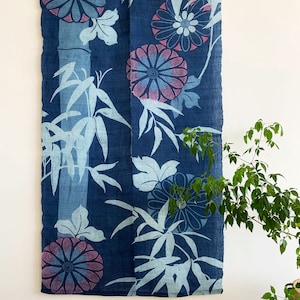 May include: A navy blue textile with a floral and bamboo design. The flowers are a combination of blue and pink, and the bamboo and leaves are light blue. The textile is hanging on a wooden rod against a white wall.