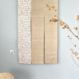 May include: A decorative wall hanging with three panels. The left panel has a white background with a brown floral pattern. The centre and right panels are a solid beige colour. The panels are suspended from a wooden rod.