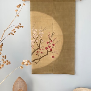 May include: A beige linen wall hanging with a floral design. The artwork features branches with white and red blossoms. The hanging is suspended from a wooden rod, creating a simple yet elegant decorative piece.