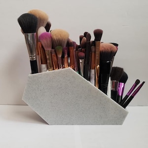 May include: A white hexagonal makeup brush holder with a textured surface, filled with a variety of makeup brushes.