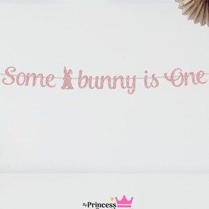 May include: Pink glitter banner with the text "Some bunny is one" and a pink glitter bunny silhouette.