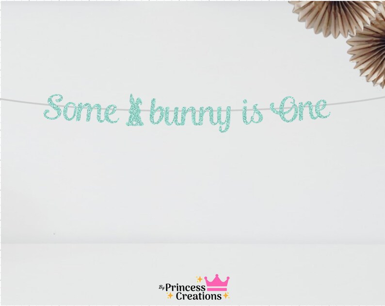 May include: A turquoise glitter banner with the text "Some bunny is One".