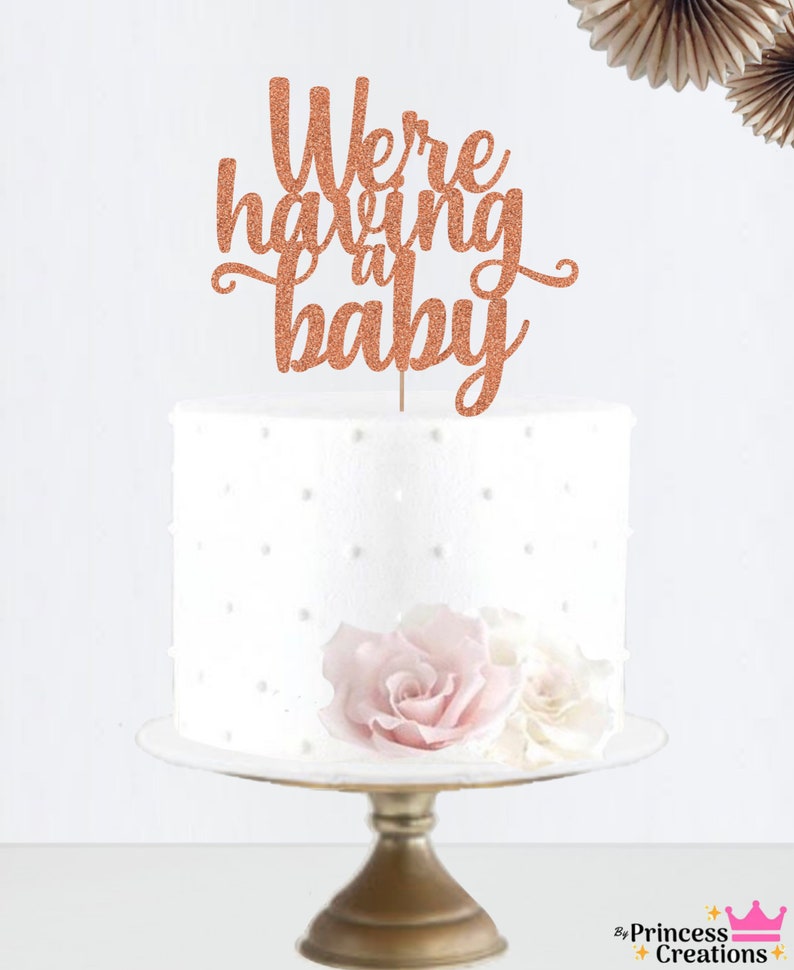 May include: Rose gold glitter cake topper with the text "We're having a baby".