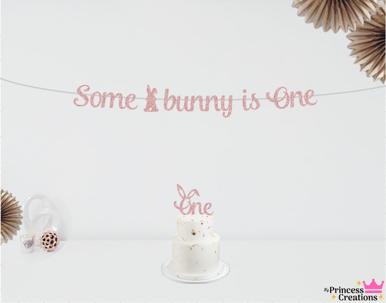 May include: Pink glitter banner with the text "Some bunny is One" and a pink glitter cake topper with the text "One" on a white cake with gold sprinkles.