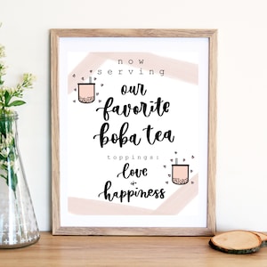 Puede incluir: Una impresi&oacute;n enmarcada con un fondo abstracto rosa y blanco. El texto dice "now serving our favorite boba tea toppings: love & happiness". La impresi&oacute;n presenta dos ilustraciones de tazas de boba tea con pajitas.