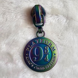 May include: A rainbow iridescent zipper pull with a circular charm that says "Platform 9 3/4 King's Cross Station".