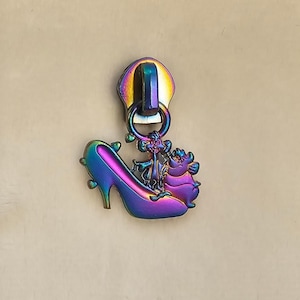 May include: A rainbow iridescent zipper pull featuring a glass slipper with two cartoon characters on top. The characters are a pig and a cat.
