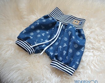 May include: Blue denim shorts with a nautical pattern of anchors, ship wheels, and diamonds. The shorts have a white drawstring, and a striped waistband and cuffs. A small tag is sewn on the waistband.