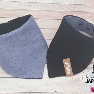 May include: Two fabric baby bibs, one blue and one black, with a brown label that says "Johan" on the black bib. The bibs are handmade and have a black trim.