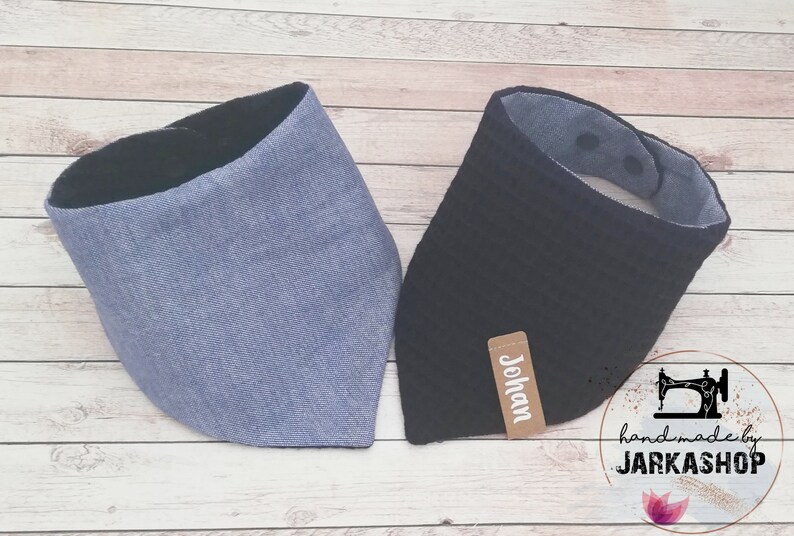 May include: Two fabric baby bibs, one blue and one black, with a brown label that says "Johan" on the black bib. The bibs are handmade and have a black trim.