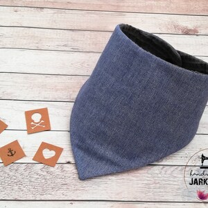 May include: A blue bandana with a dark gray lining. The bandana is made of a soft, textured fabric. The bandana is on a wooden surface with four small brown squares with white symbols on them. The squares have a star, a skull and crossbones, an anchor, and a heart. The text "handmade by JARKASHOP" is visible in the lower right corner of the image.
