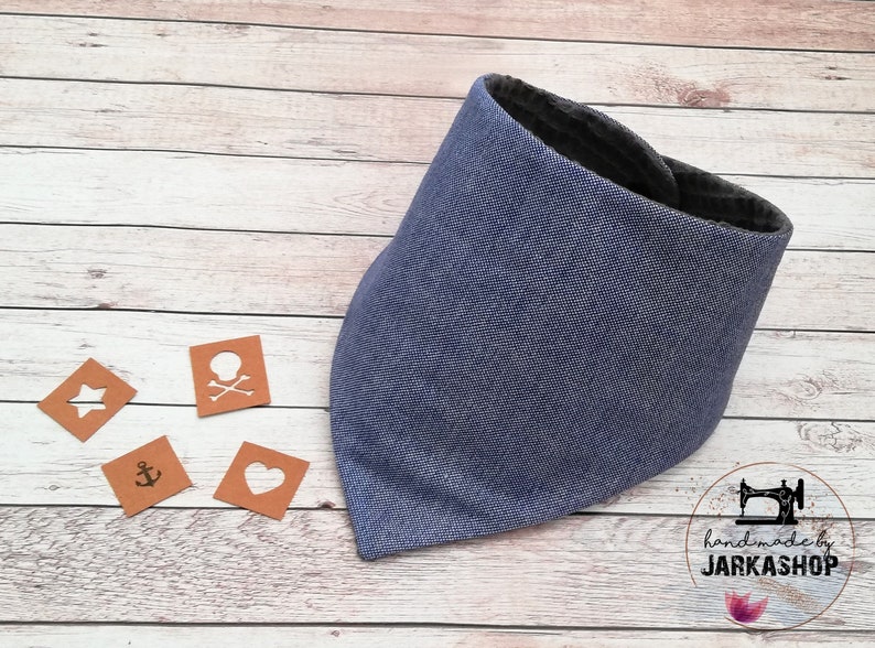 May include: A blue bandana with a dark gray lining. The bandana is made of a soft, textured fabric. The bandana is on a wooden surface with four small brown squares with white symbols on them. The squares have a star, a skull and crossbones, an anchor, and a heart. The text "handmade by JARKASHOP" is visible in the lower right corner of the image.